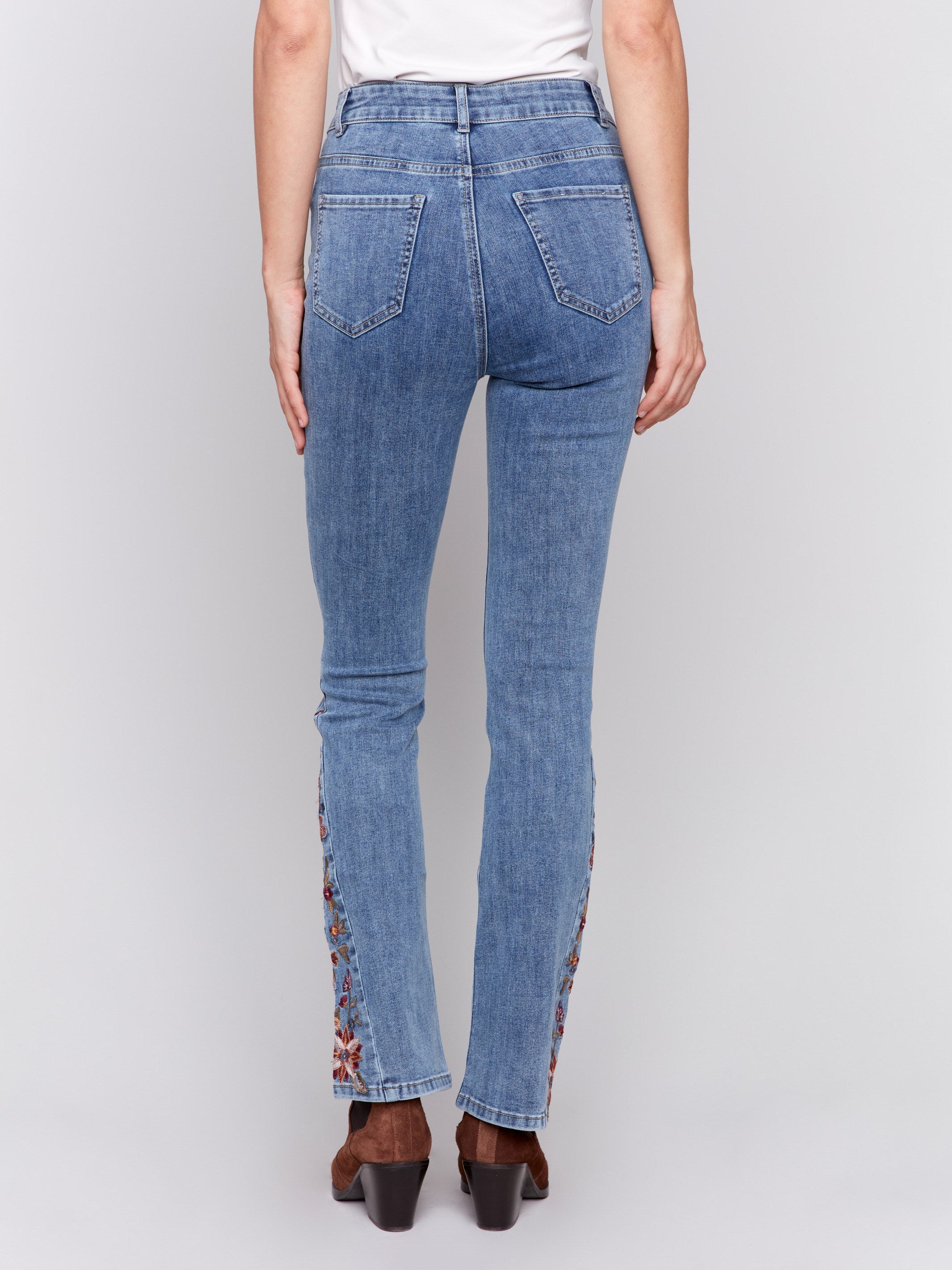 Medium blue bootcut jeans with vibrant floral embroidery on the sides and a classic five-pocket design by Charlie B.