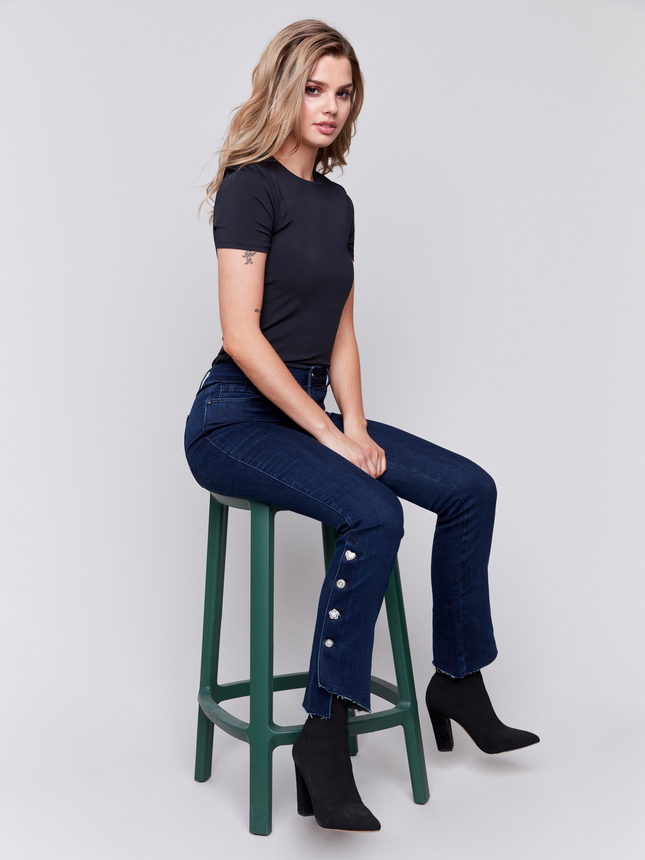 Dark blue-black bootcut jeans with gem buttons and a raw edge hem, featuring a five-pocket design by Charlie B.