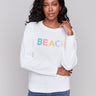 White sweater featuring a colorful 'BEACH' graphic design by Charlie B.