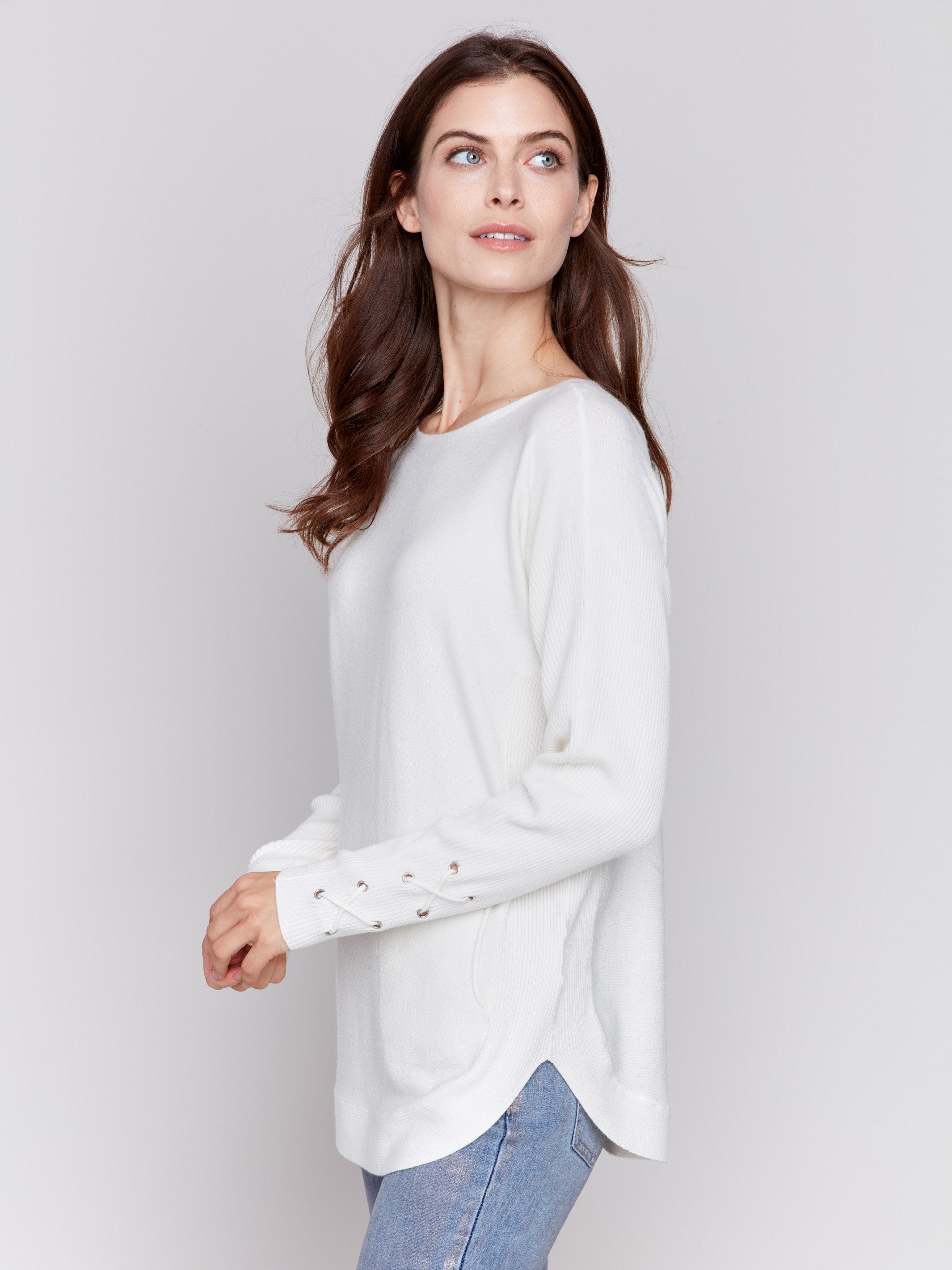 Ecru white long-sleeved knit sweater with lace-up cuffs, rounded hem, and front pockets by Charlie B.