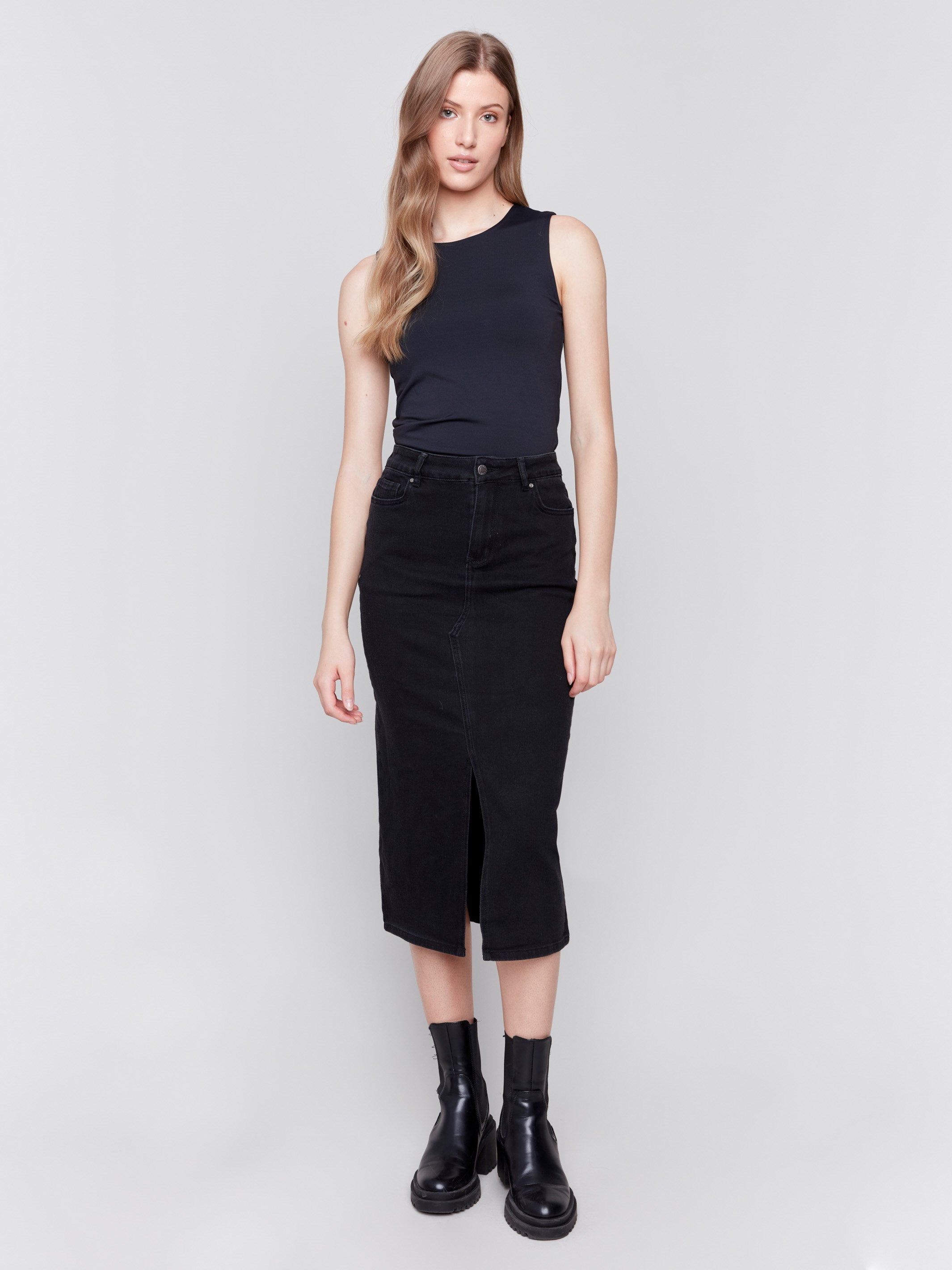 Charcoal black midi-length denim skirt with front slit, featuring a mid-rise waist and slim fit, paired with boots by Charlie B.