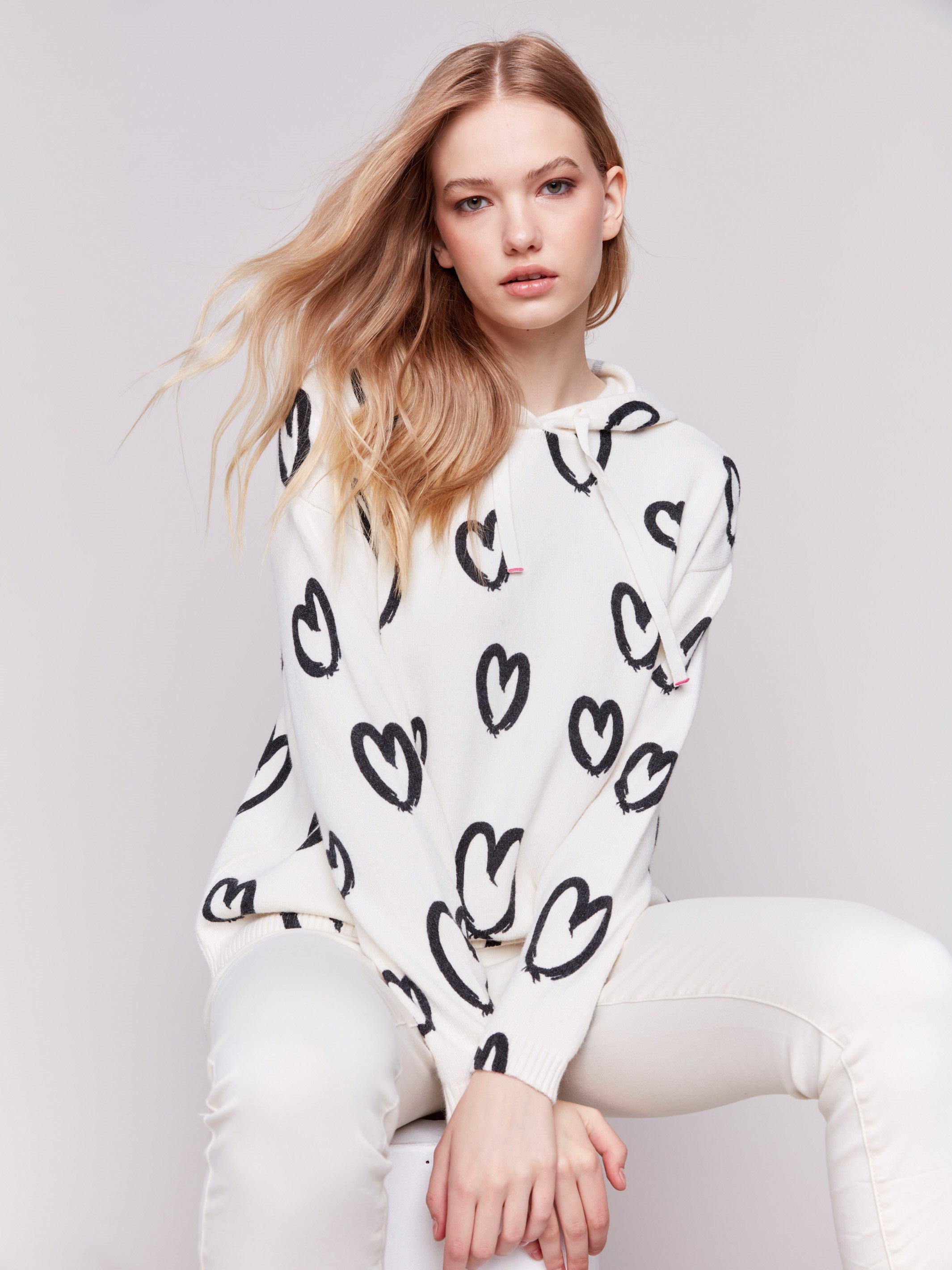 Stylish white hoodie sweater with black heart prints, featuring a drawstring hood and raglan sleeves by Charlie B.