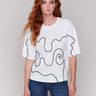 White t-shirt with drop shoulder design and black soutache accents by Charlie B.