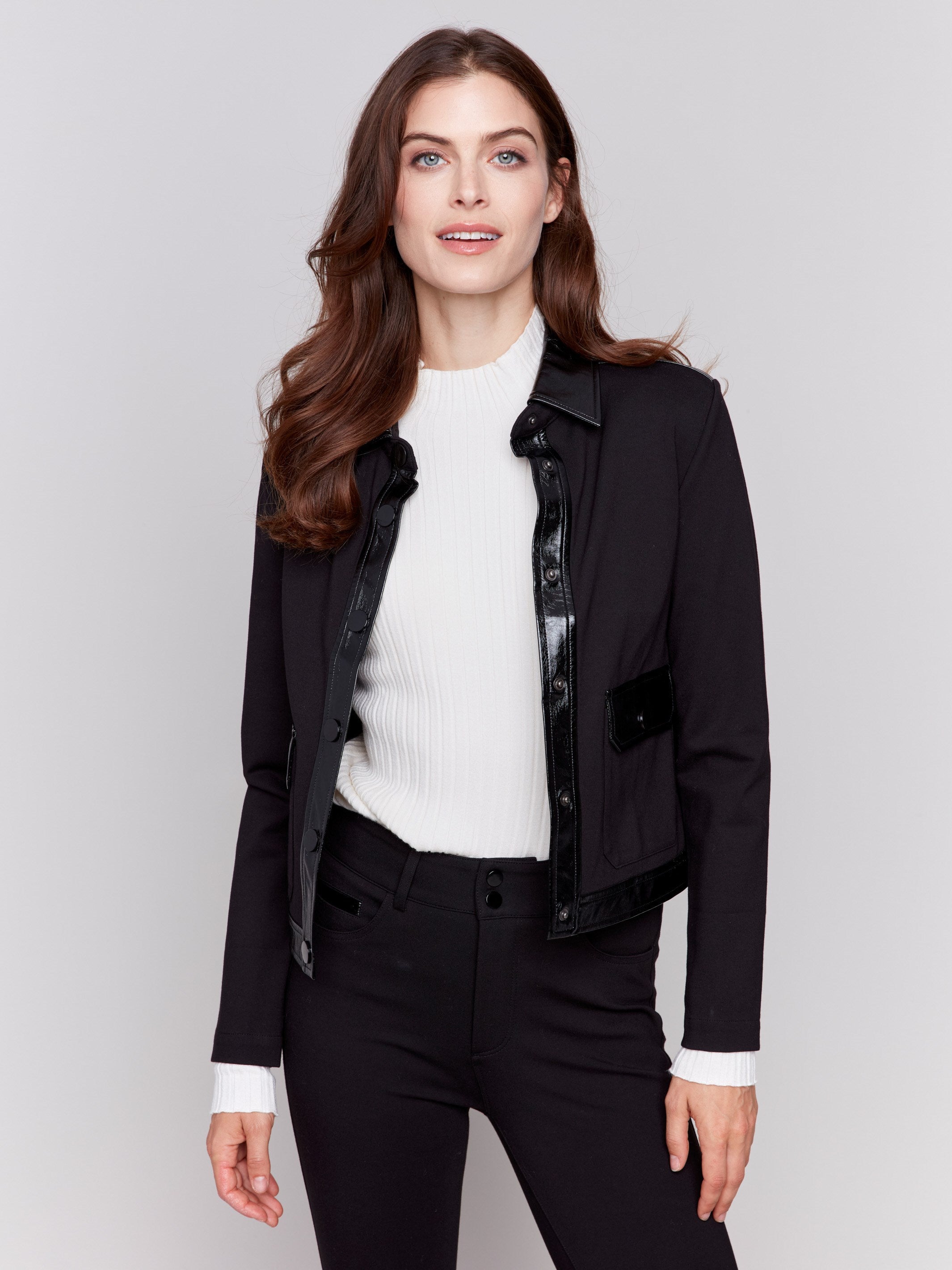 Short black jacket with glossy vinyl trim, featuring front flap pockets and a button closure, by Charlie B.