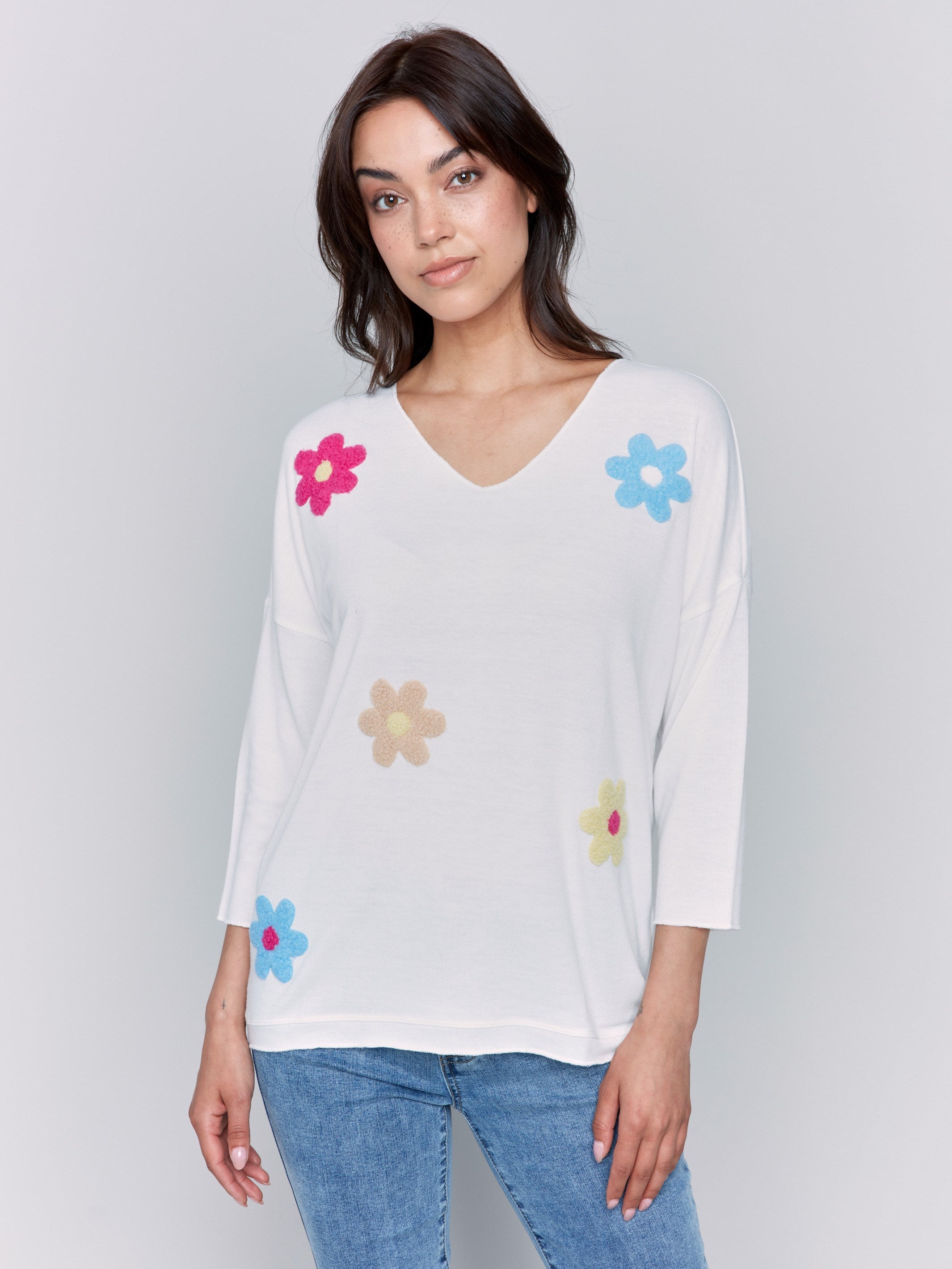 White V-neck knit top with colorful floral appliqués, featuring drop shoulders, by Charlie B.